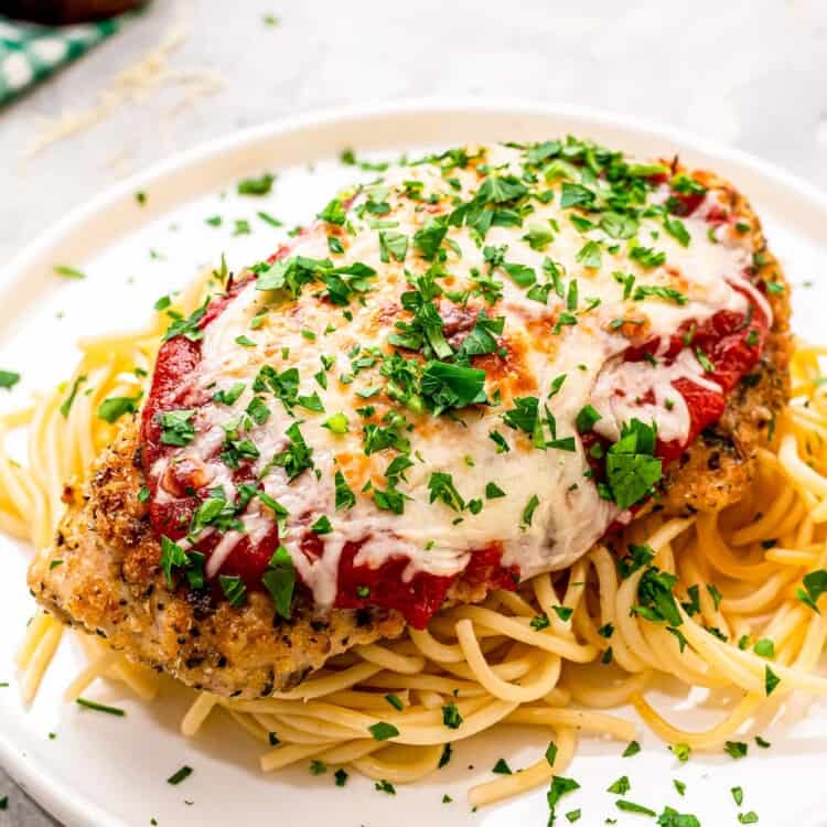 Baked Chicken Parmesan on a bed spaghetti on a white plate