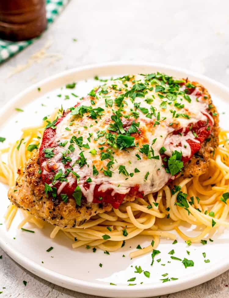 Baked Chicken Parmesan on a bed spaghetti on a white plate
