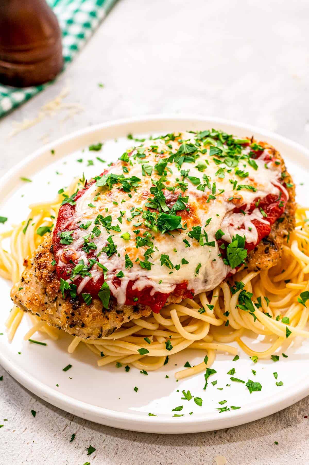 Baked Chicken Parmesan on a bed spaghetti on a white plate