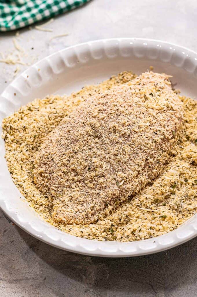 White shallow dish with breadcrumbs and chicken breast