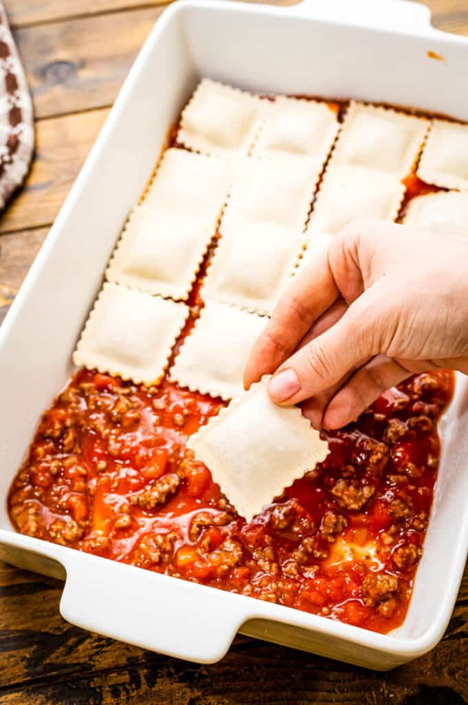 Hand putting cheese ravioli into casserole pan