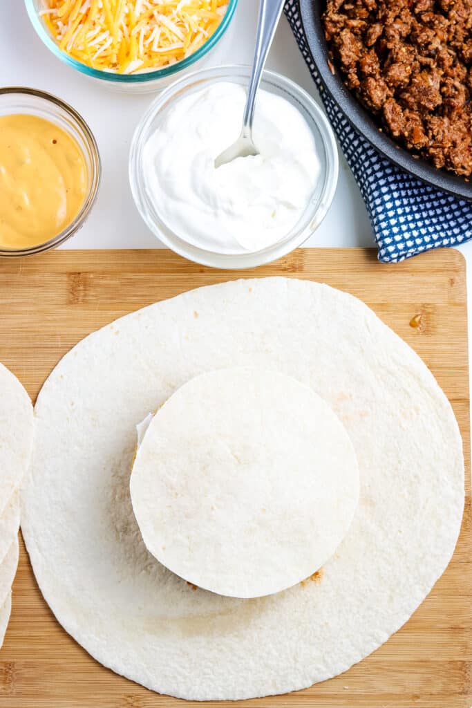 Round flour tortilla laying on top of softshell with crunchrwap ingredients