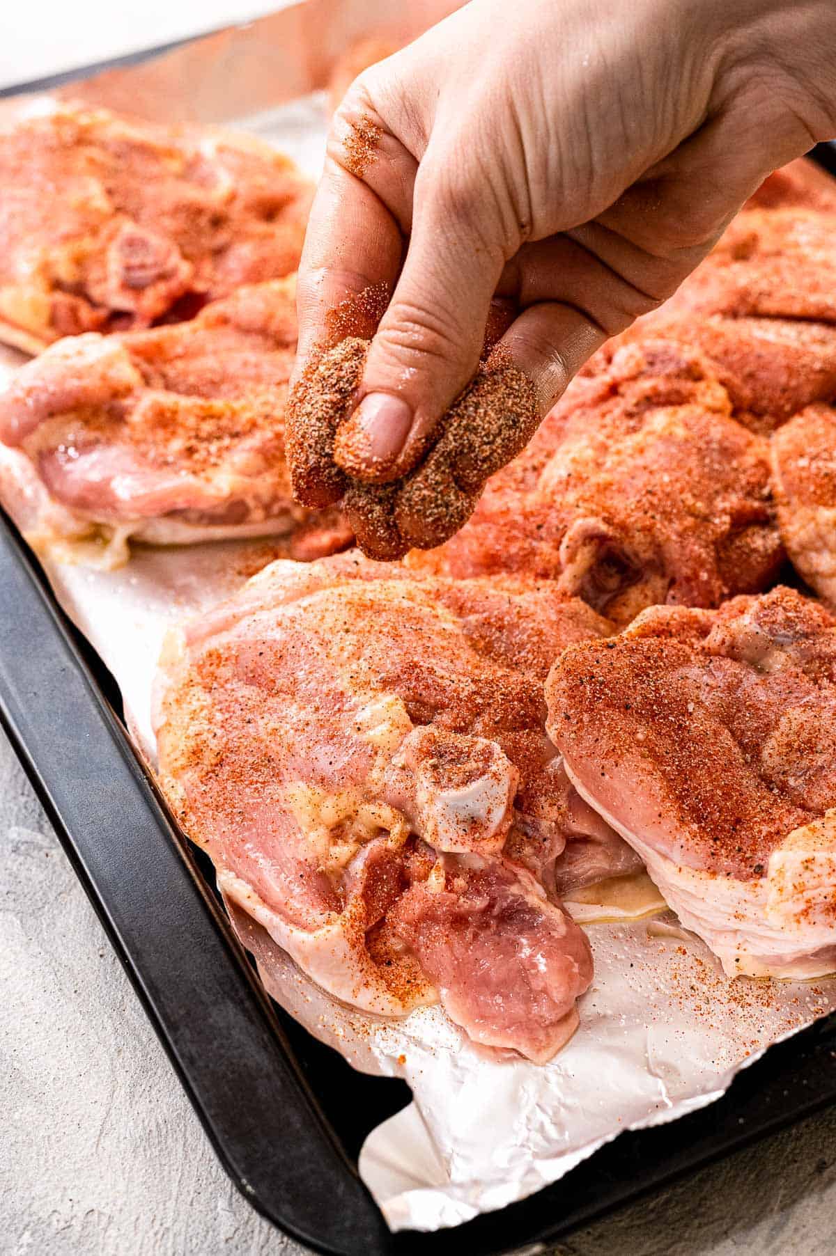 Hand sprinkling seasoning onto raw chicken thighs