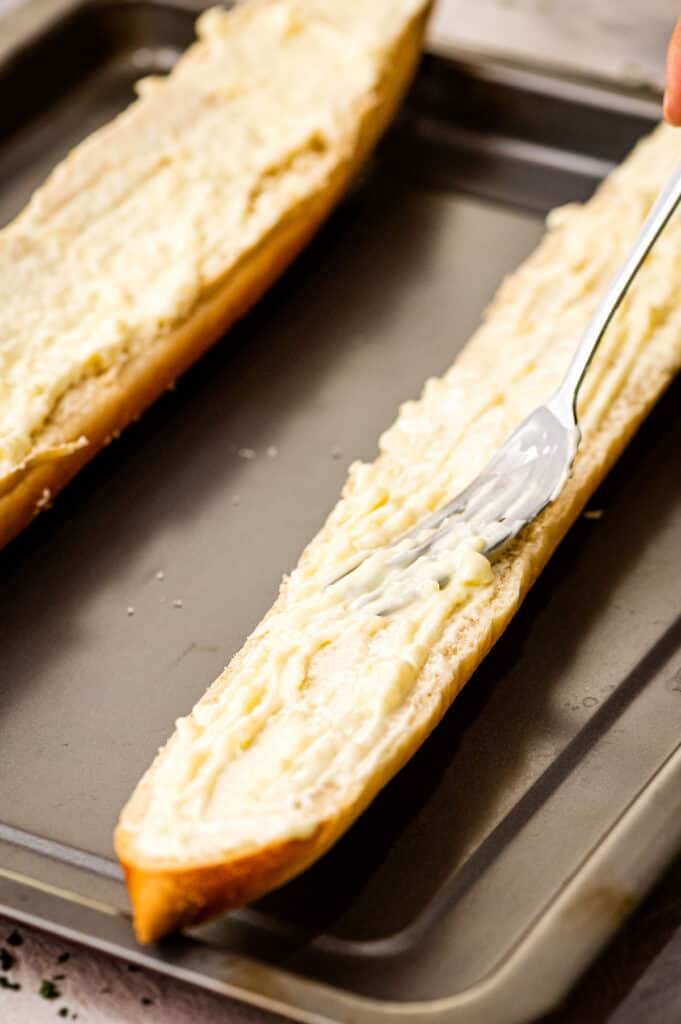 Fork spreading softened butter on French Bread