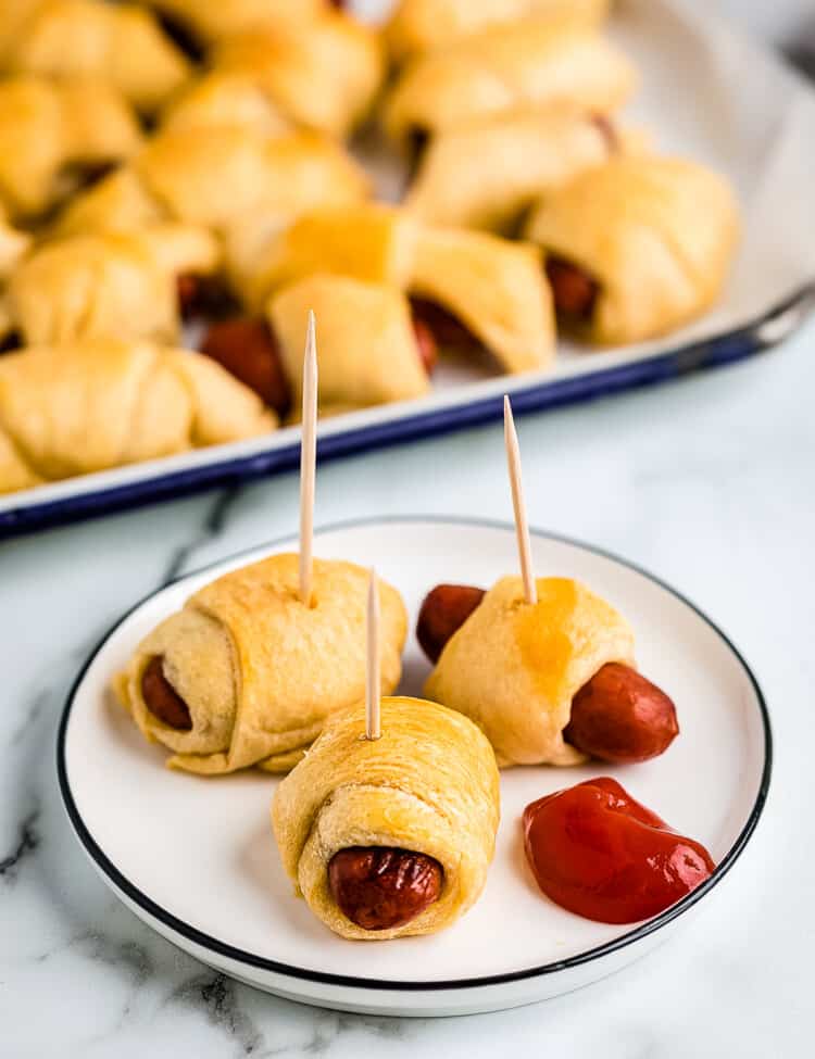 Plate with pigs in a blanket with toothpicks in them and ketchup