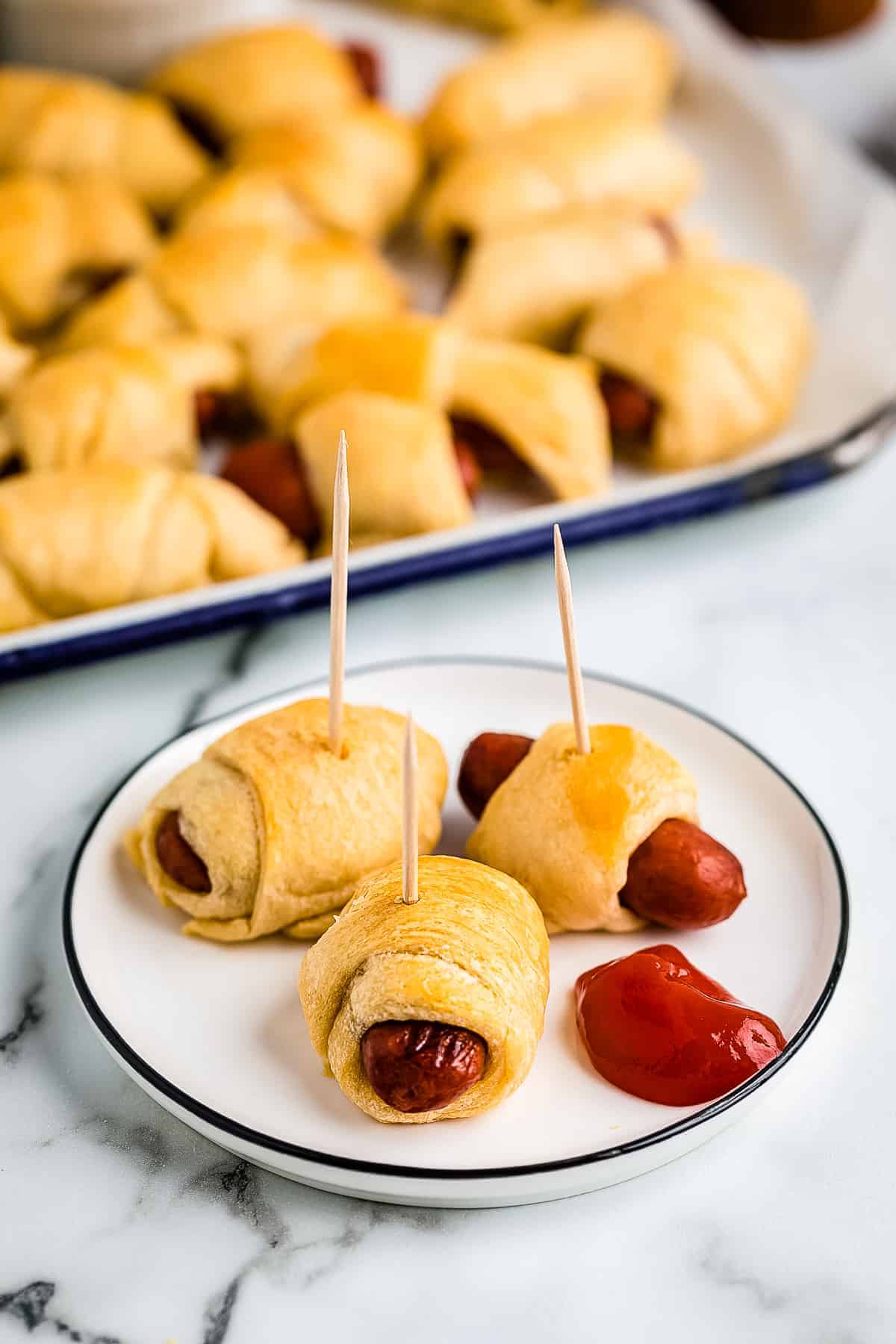 Plate with pigs in a blanket with toothpicks in them and ketchup