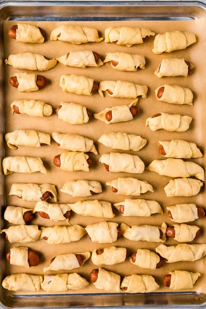 An overhead image of unbaked pigs in a blanket on sheet pan