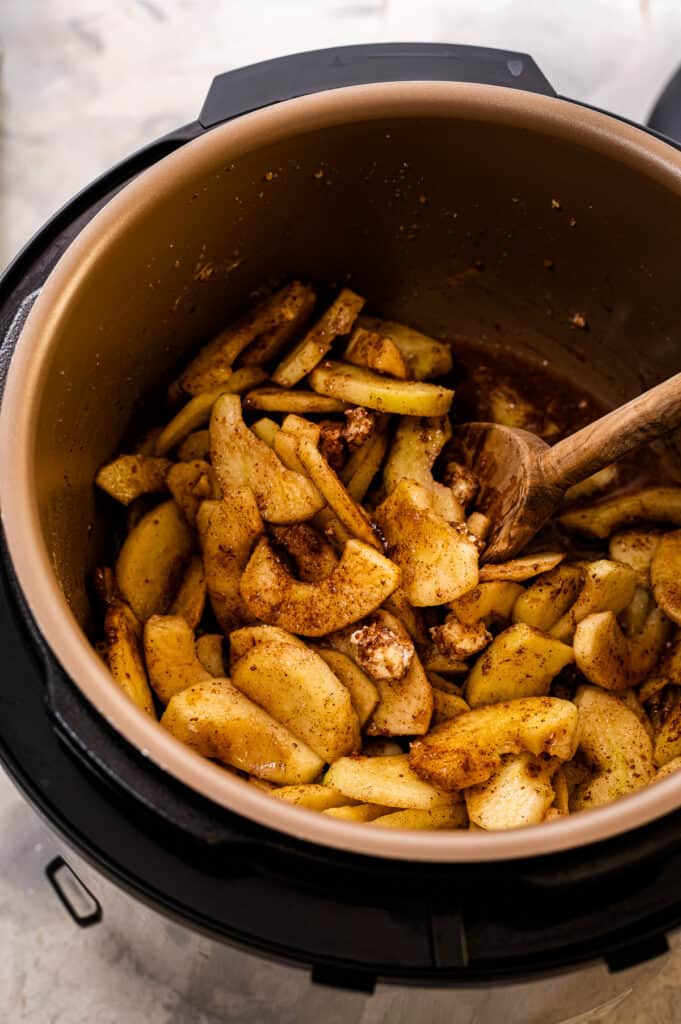 Wooden spoon stirring cinnamon apples ingredients in Instant Pot