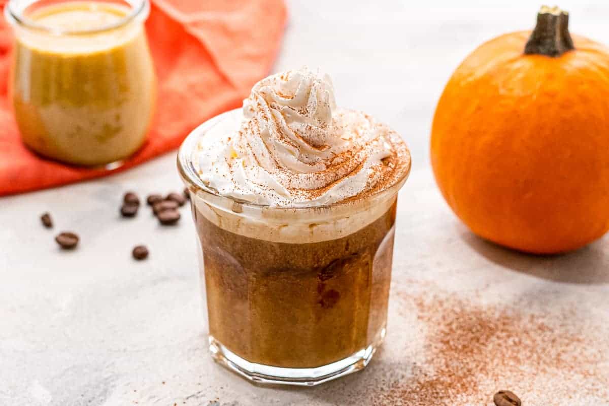 Glass with coffee in it and pumpkin spice creamer topped with whipped cream