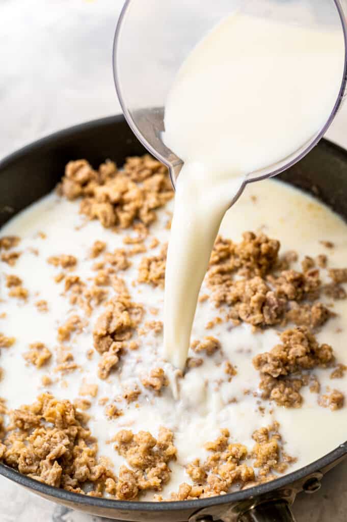 Pouring milk over sausage in skillet