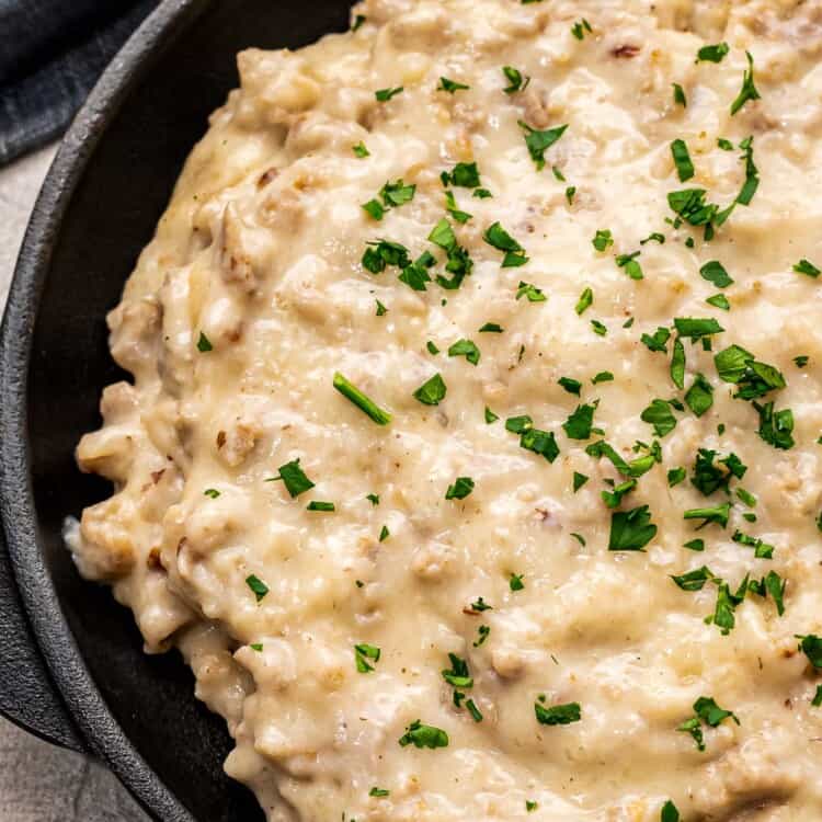 Black skillet with sausage gravy topped with chopped parsley