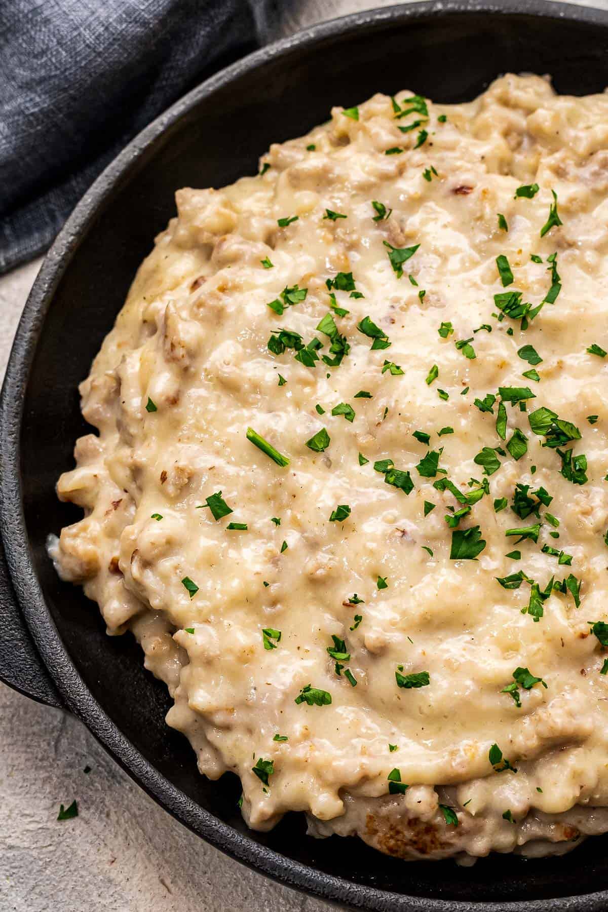 Black skillet with sausage gravy topped with chopped parsley