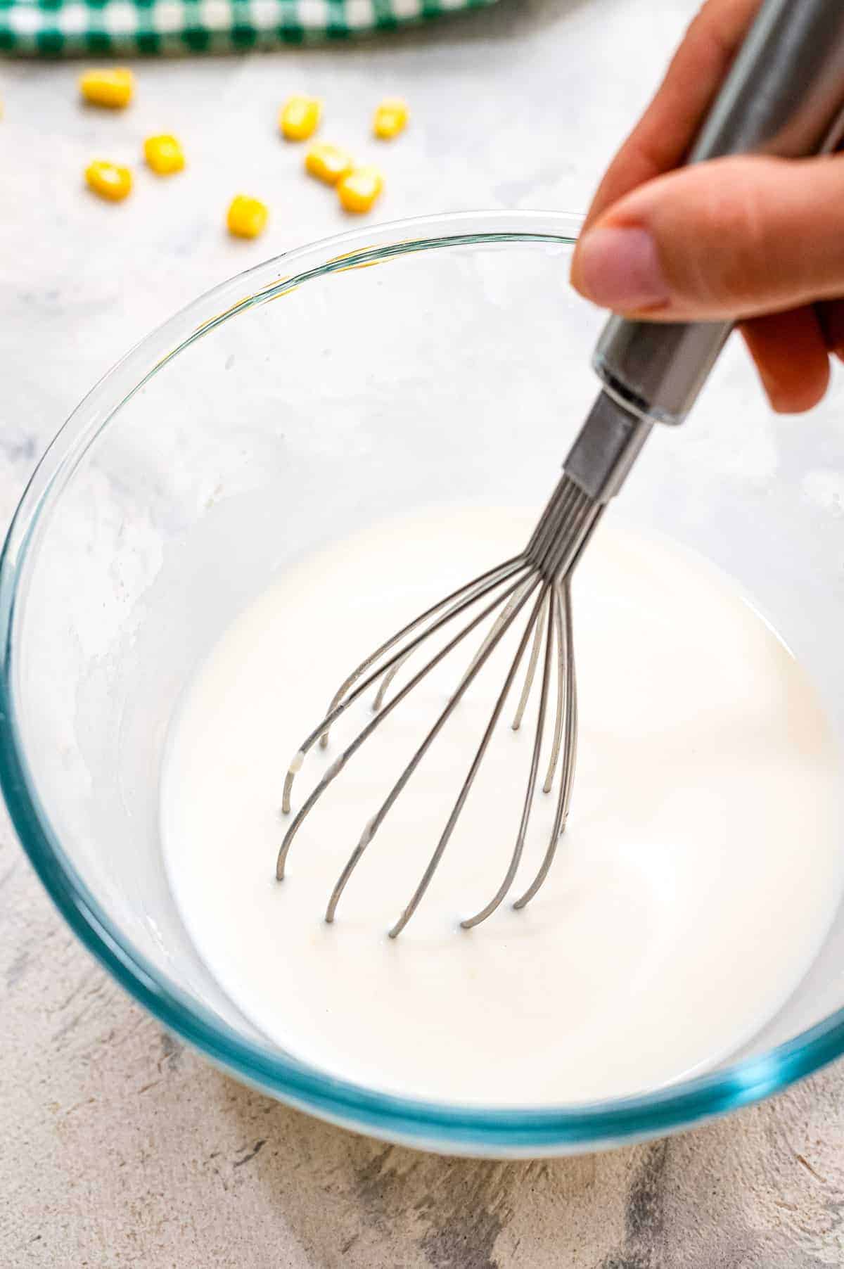 Glass bowl with milk and flour being whisked together