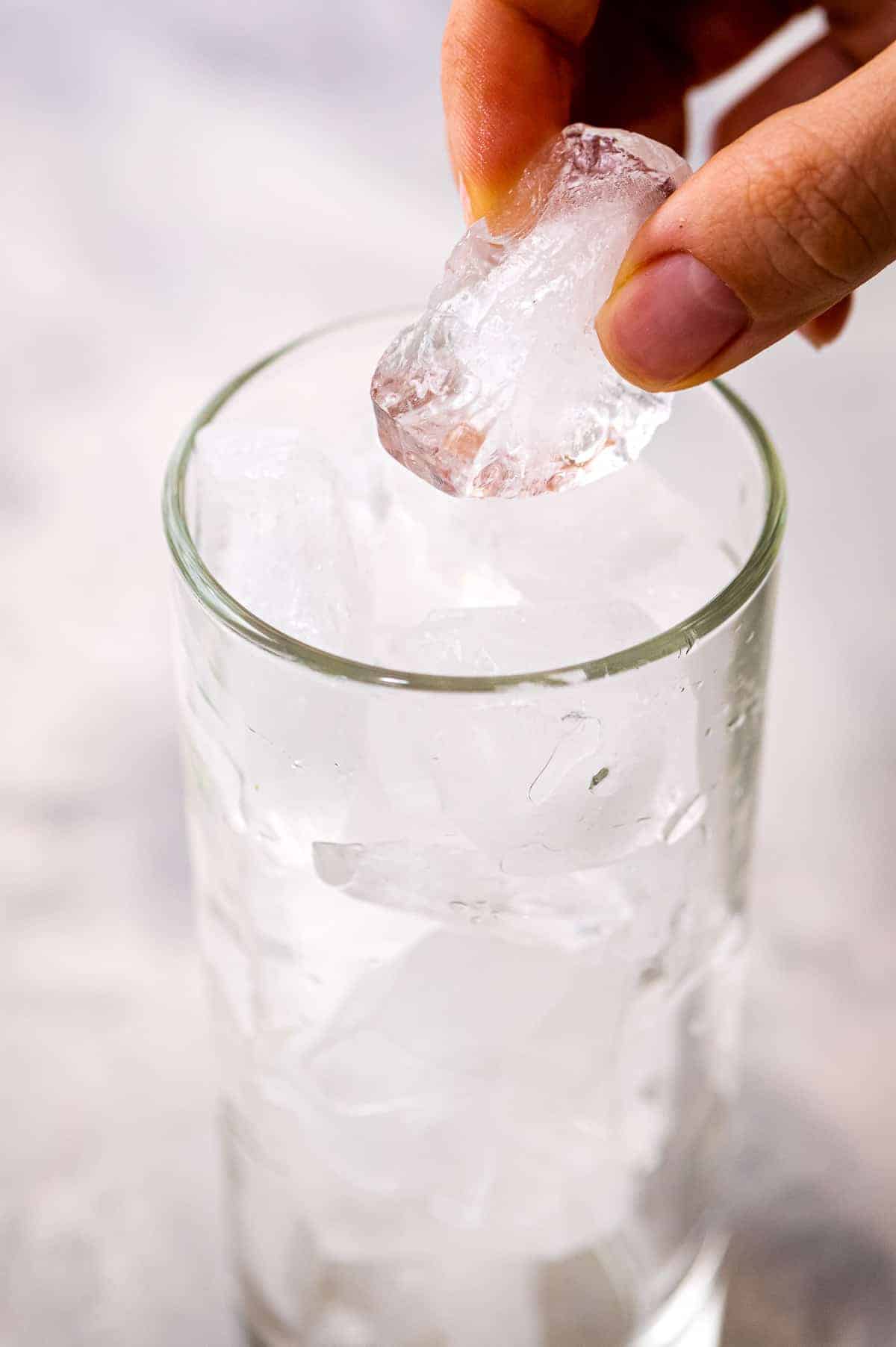 Hand putting ice cubes into a highball glass