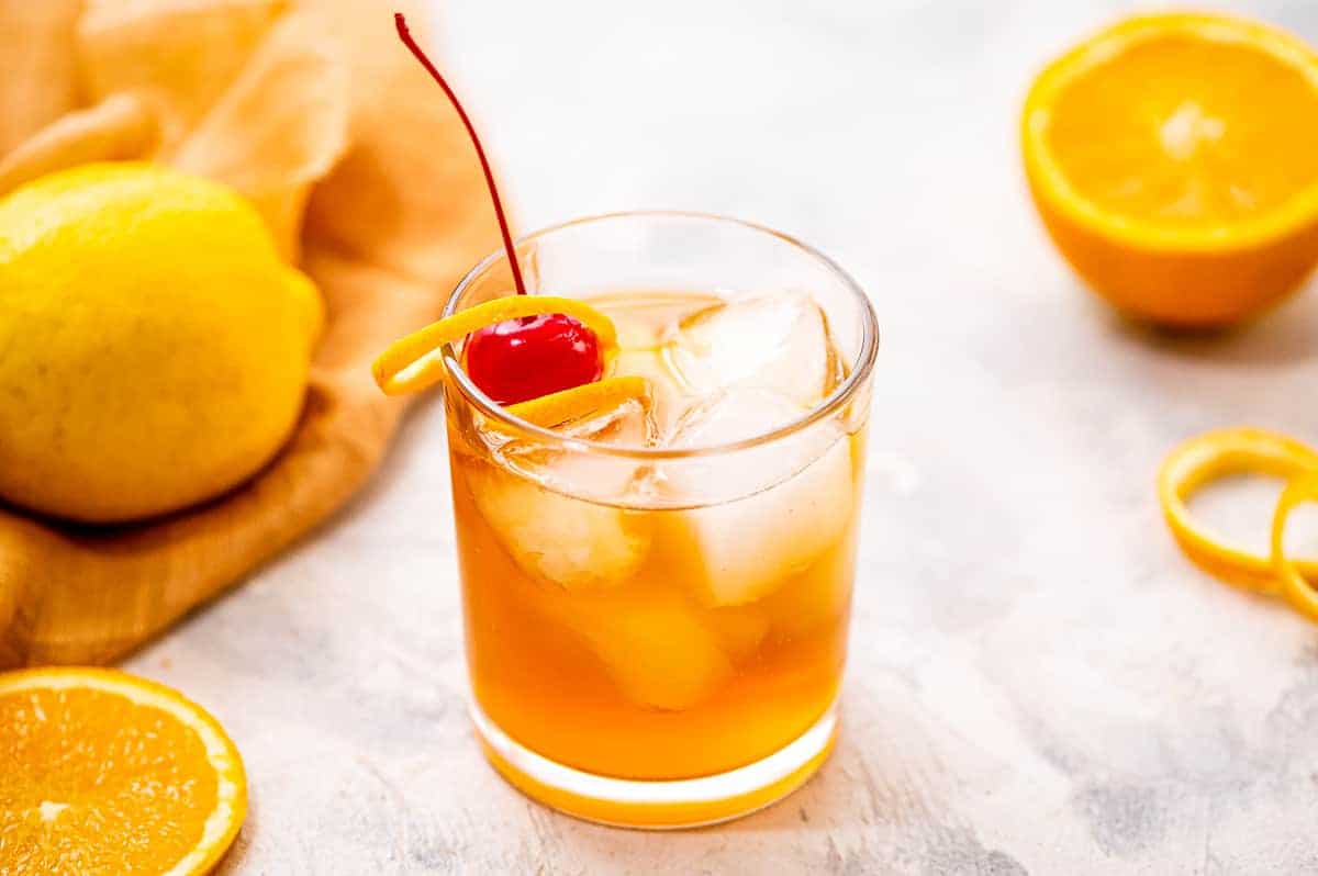 Cocktail glass with whiskey sour in it and garnished with maraschino cherry and orange peel