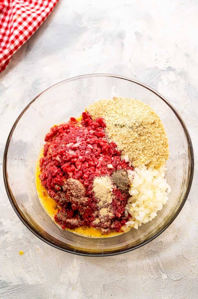 Ground beef mixture with seasoning and breadcrumbs in glass bowl