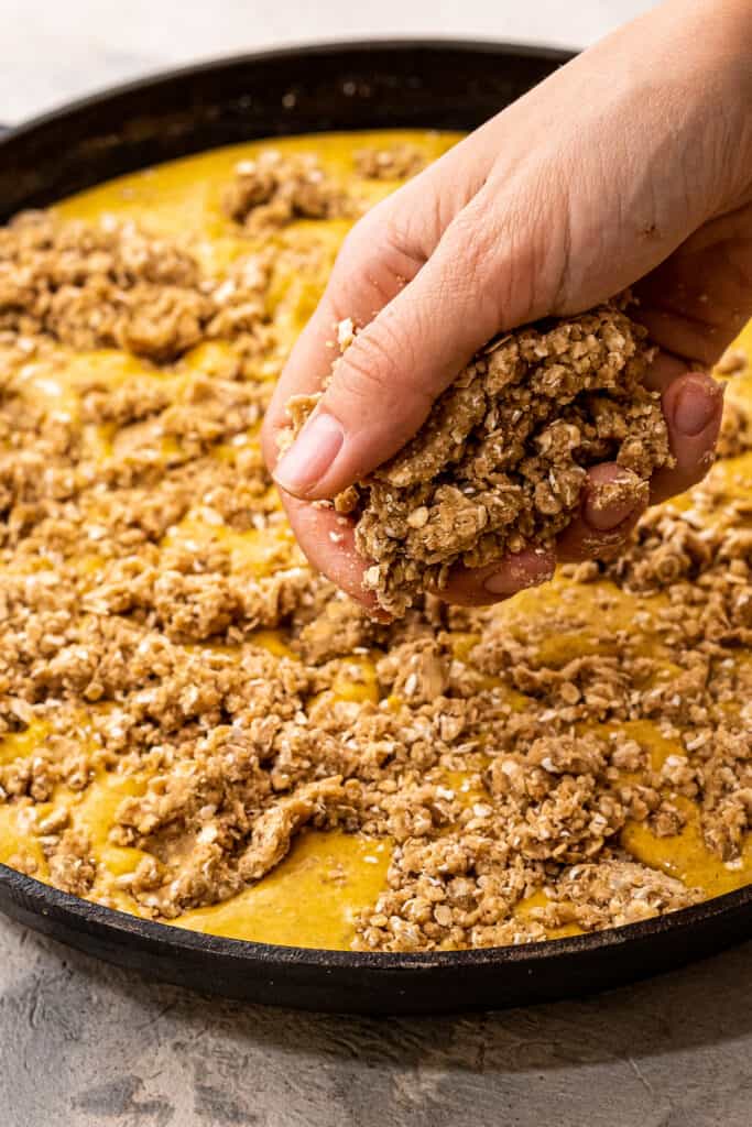 Hand sprinkling streusel topping over pumpkin filling