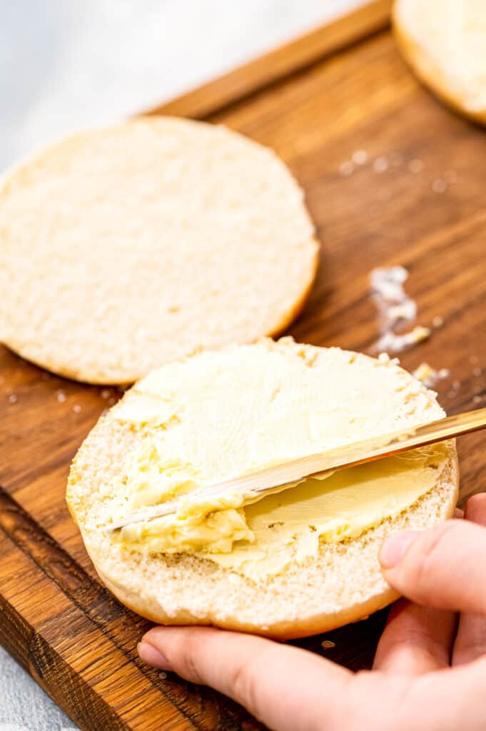 Hand putting butter on inside of bun with butter knife