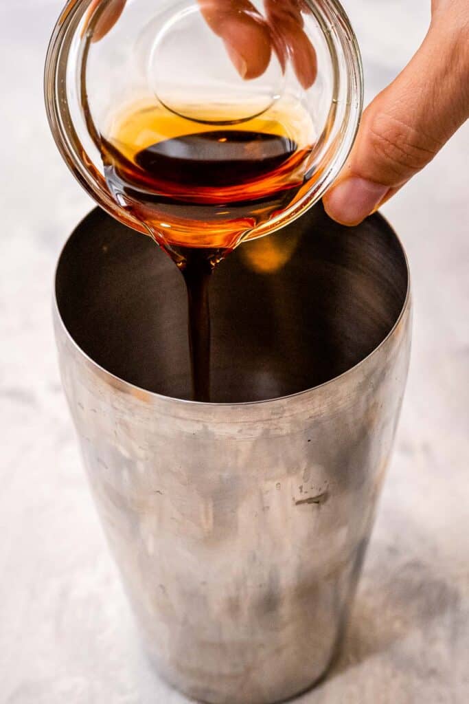 Hand pouring maple syrup into cocktail shaker