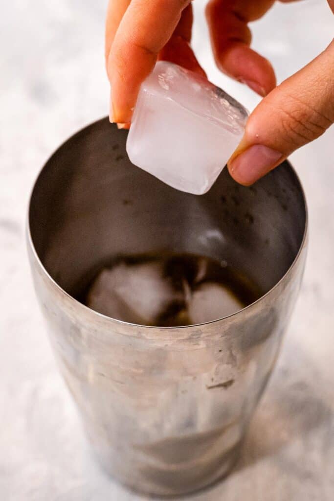 Hand putting ice cubes into cocktail shaker