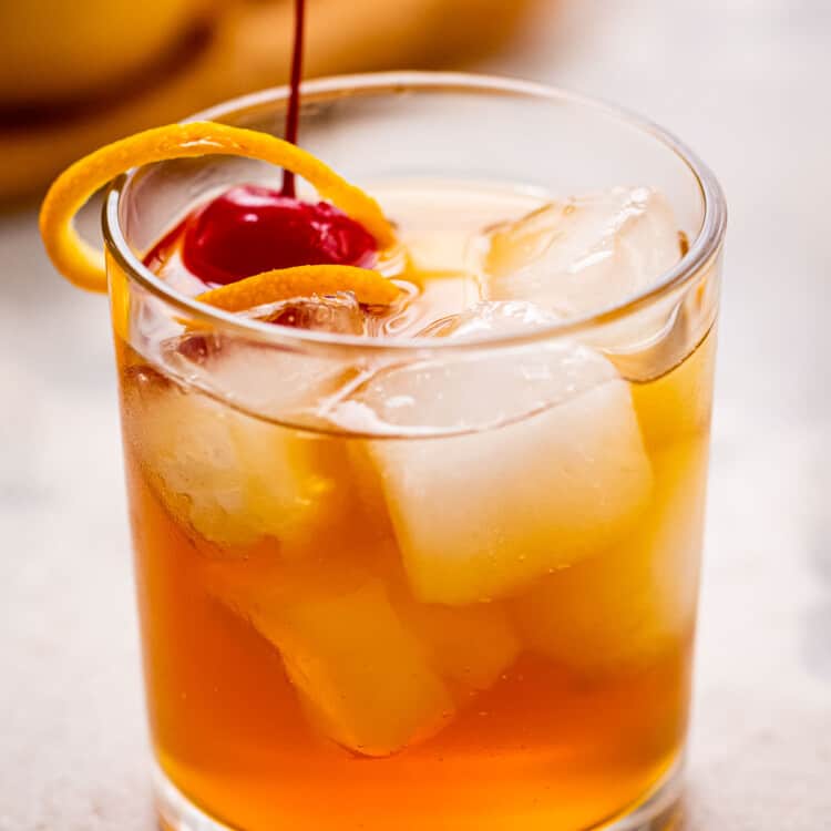 Glass with whiskey sour garnished with orange peel and maraschino cherry