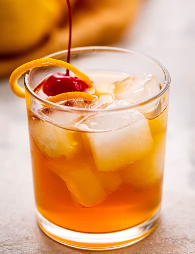 Glass with whiskey sour garnished with orange peel and maraschino cherry