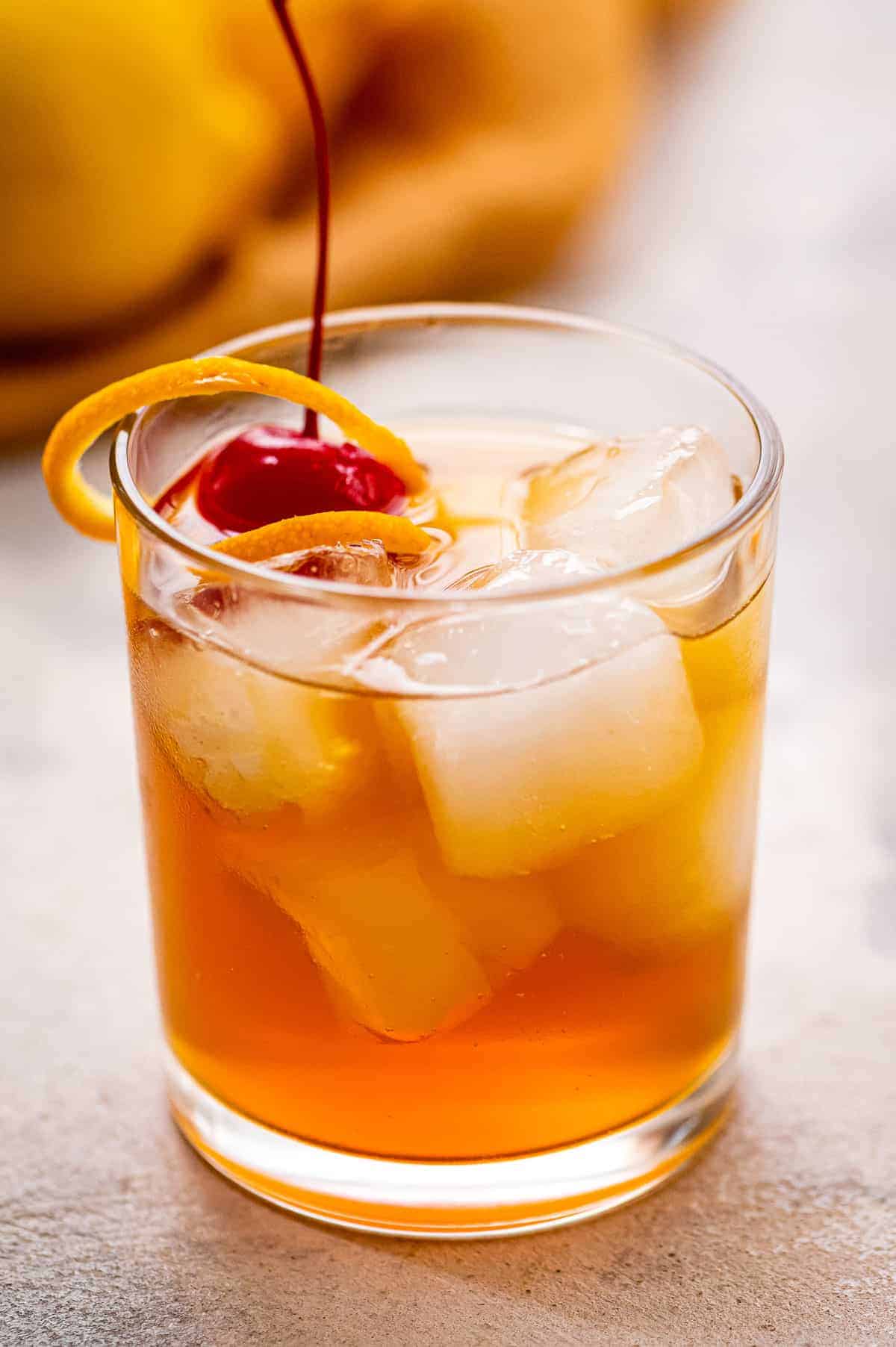 Glass with whiskey sour garnished with orange peel and maraschino cherry