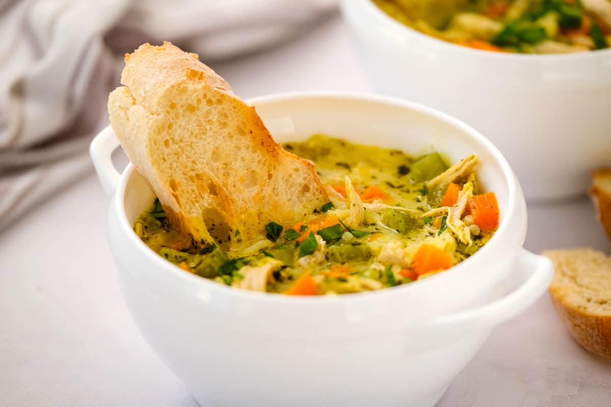 White bowl with turkey and rice soup with a piece of bread dunked in it