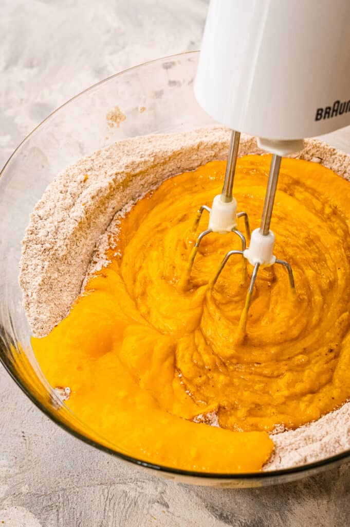 Glass bowl with pumpkin mixture for muffins and mixer mixing it