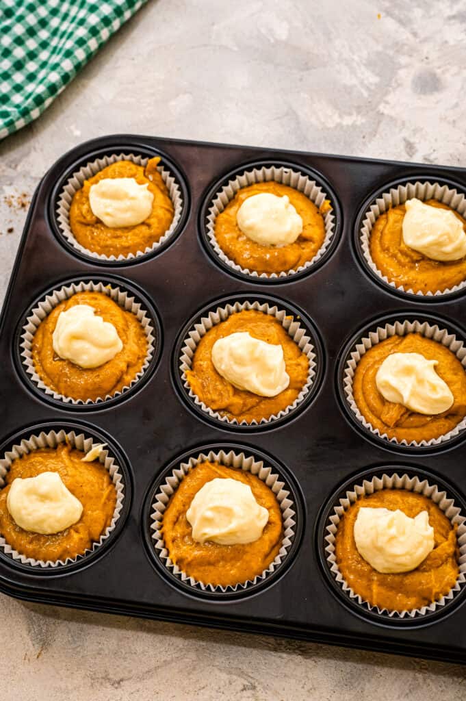Muffin tin with pumpkin muffin batter and a dollop of cream cheese on top