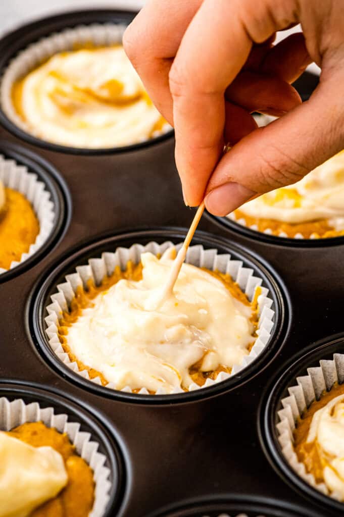 Swirling cream cheese in a pumpkin muffin with toothpick