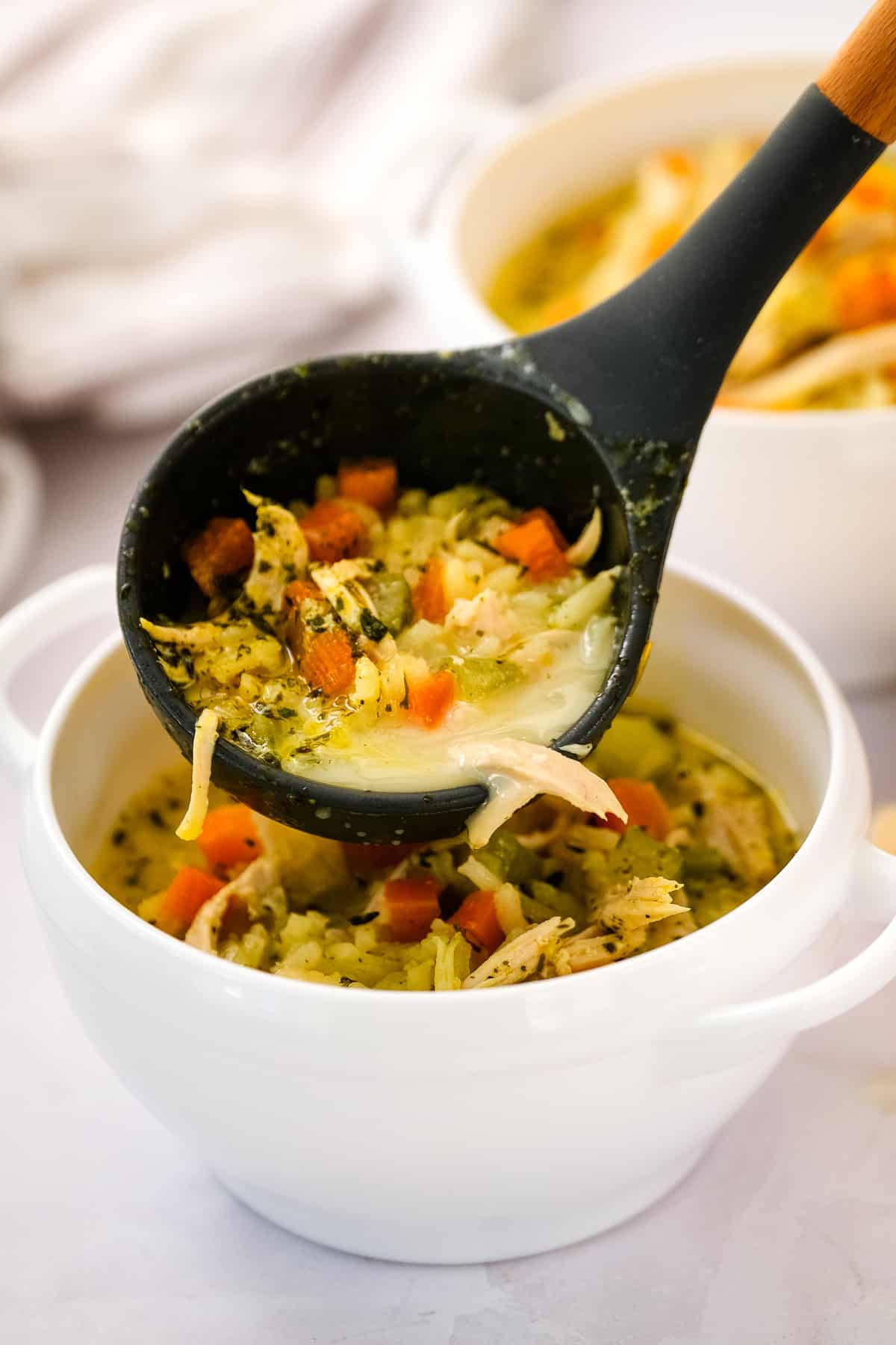 Ladle pouring turkey and rice soup into white bowl