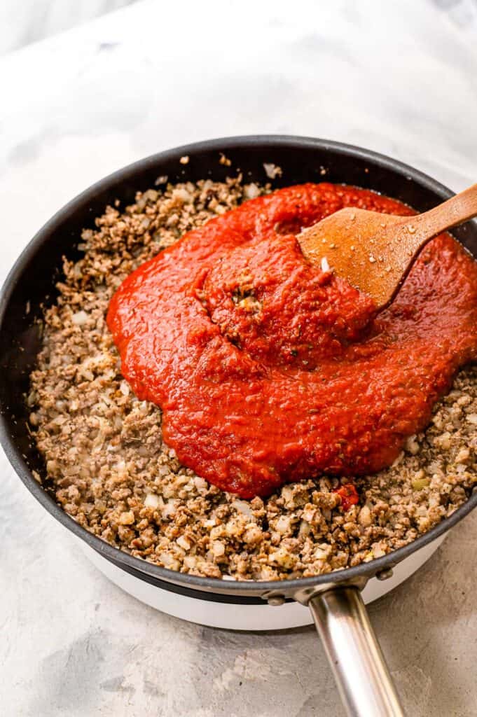 Adding marinara sauce to skillet with sausage and onions