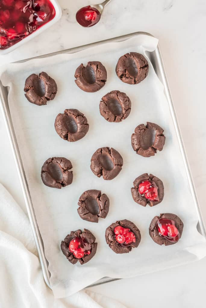 Chocolate Thumbprint Cookies on baking sheet with cherry pie filling being added