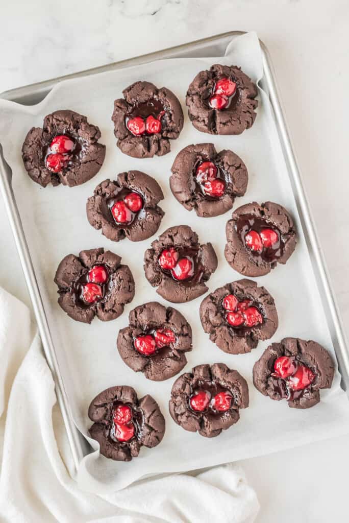 Baking sheet with chocolate cherry thumbprint cookies on it before baking