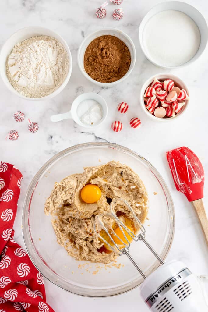 Glass mixing bowl with creamed mixture and hand mixer adding eggs