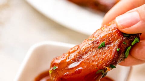 Hand dipping crock pot chicken wing in BBQ sauce