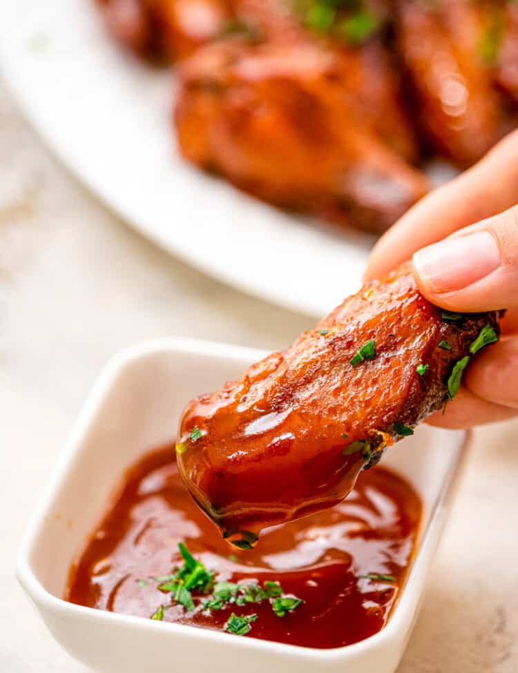 Hand dipping crock pot chicken wing in BBQ sauce