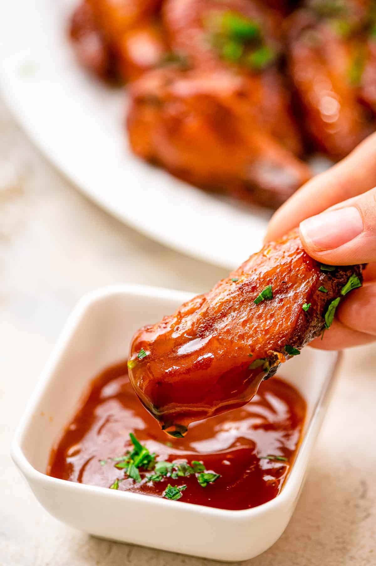 Hand dipping crock pot chicken wing in BBQ sauce