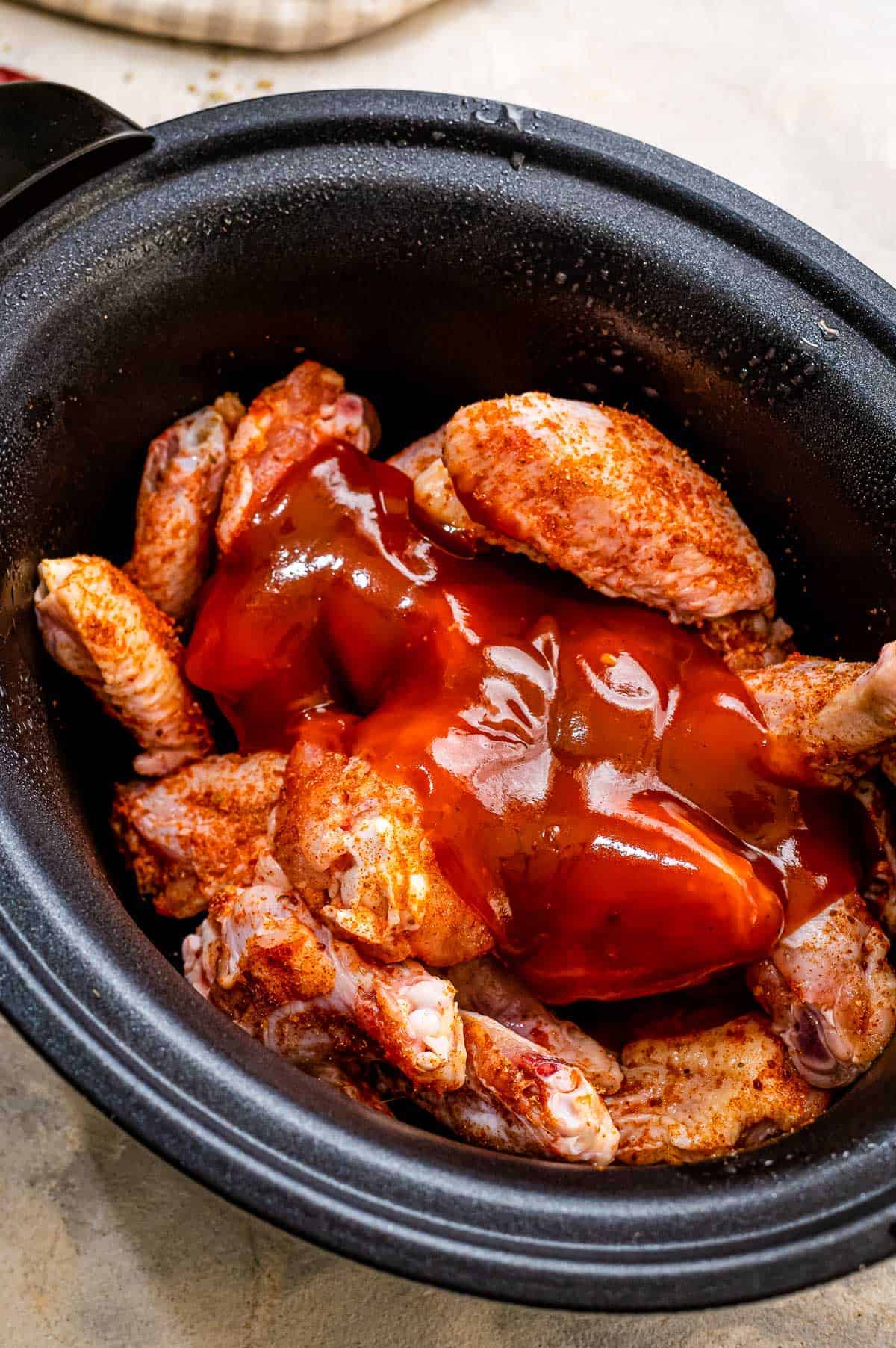 Crock pot with seasoned chicken wings and BBQ sauce
