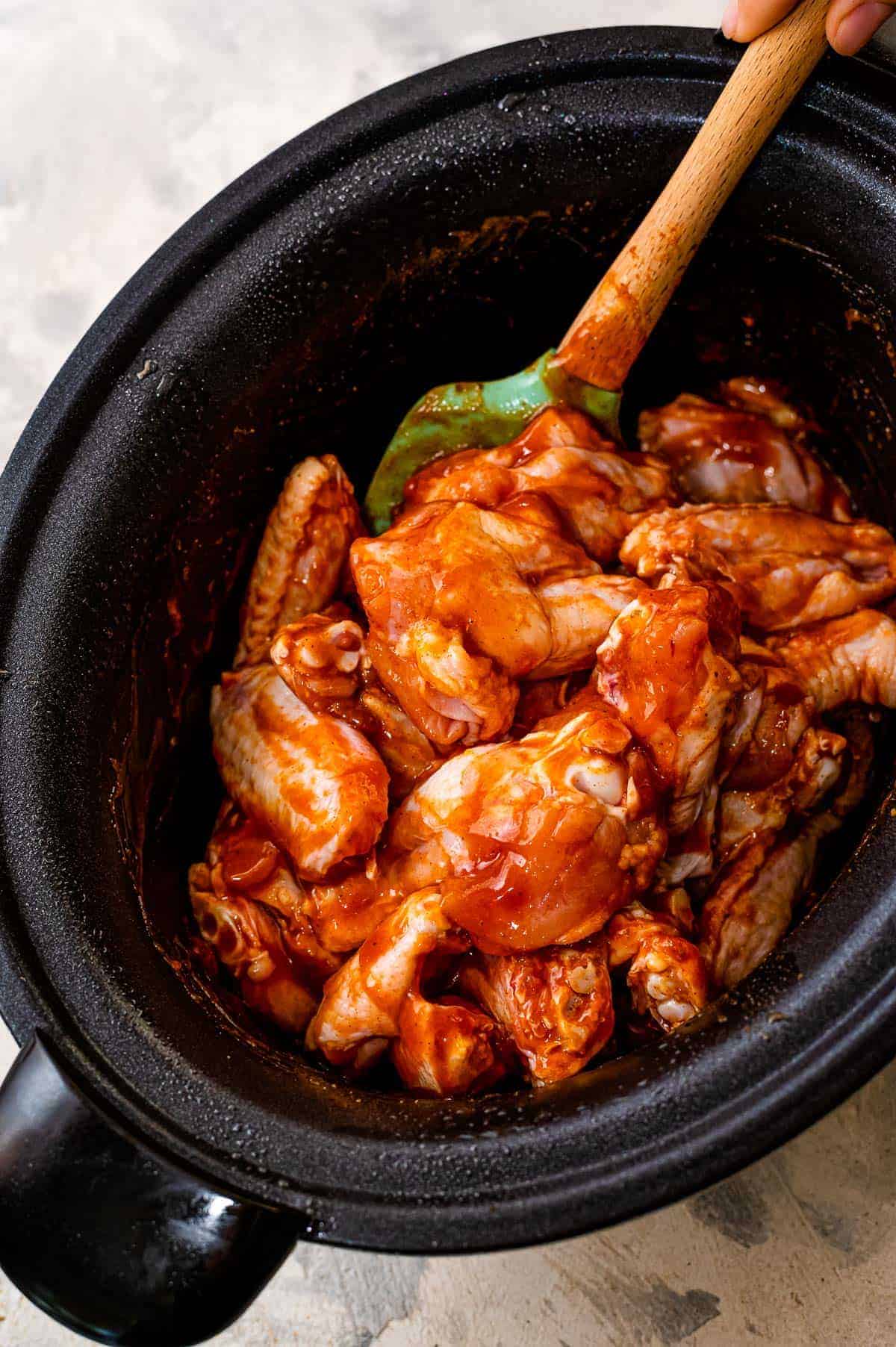Stirring chicken wings and bbq sauce in crock pot