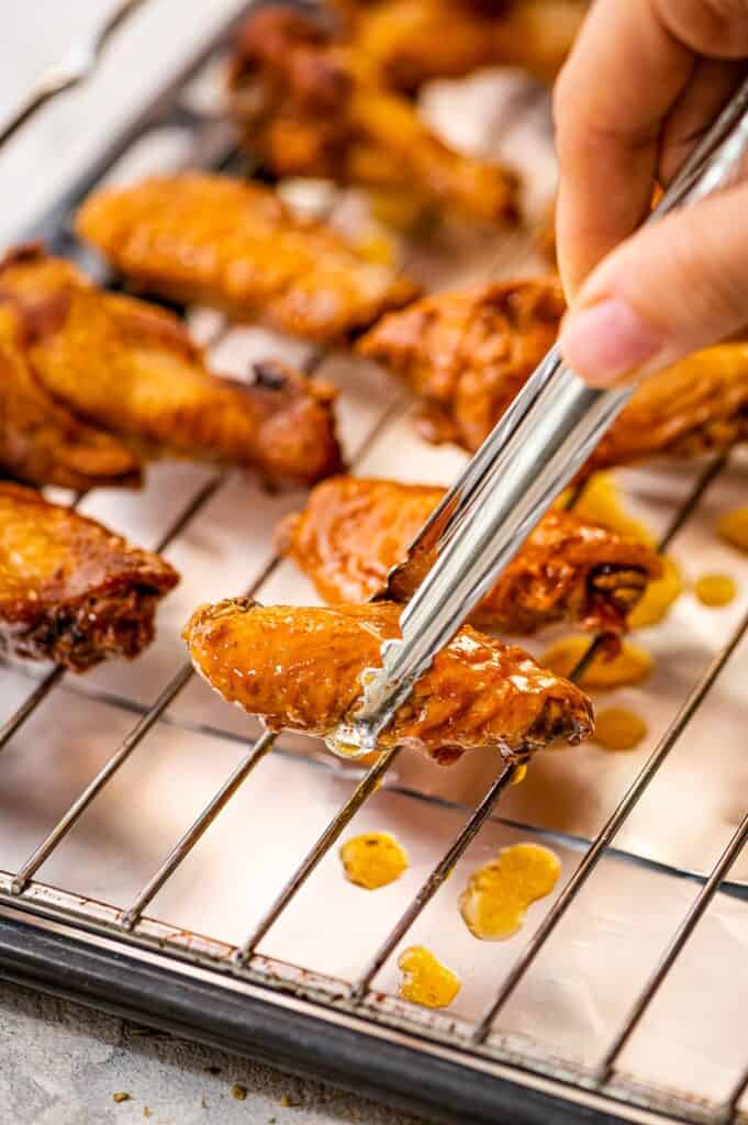 Tongs placing chicken wing on wire rack on lined sheet pan