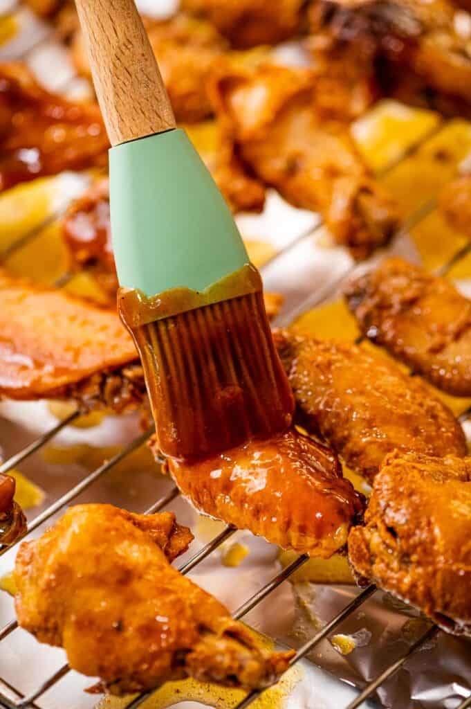 Basting brush putting bbq sauce on chicken wing on wire rack