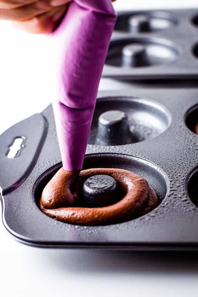Piping chocolate donut batter into donut pan cavities