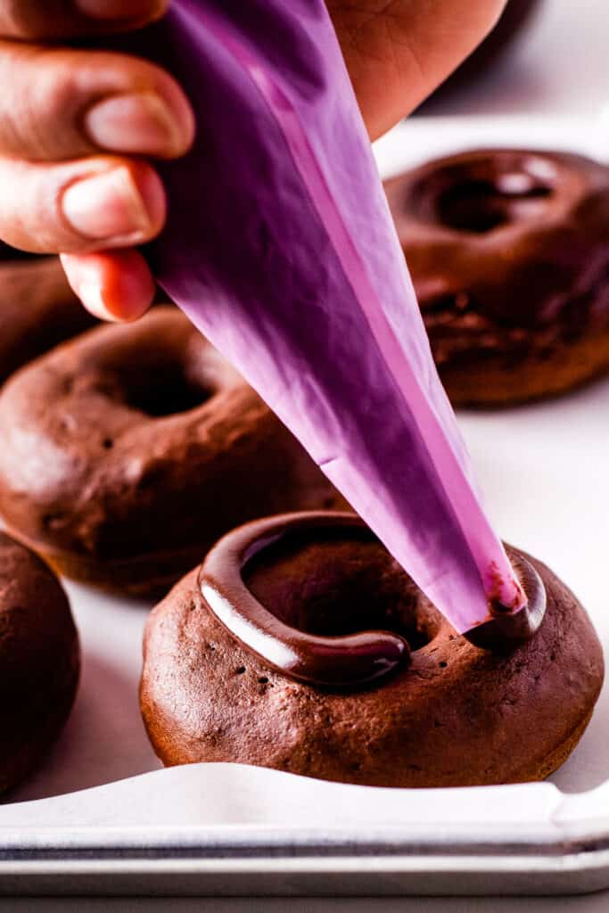 Piping chocolate frosting on chocolate donuts