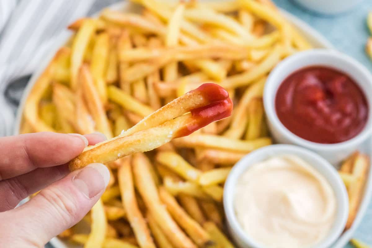 Hand holding two French Fries with ketchup