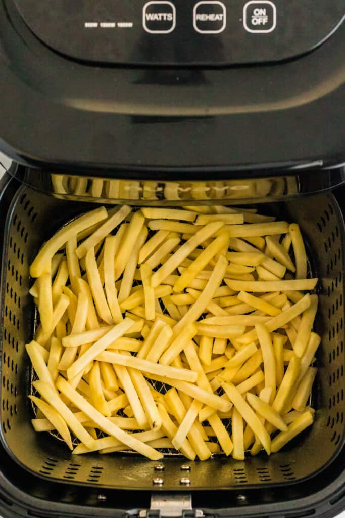 Air Fryer Basket with raw frozen French Fries in it
