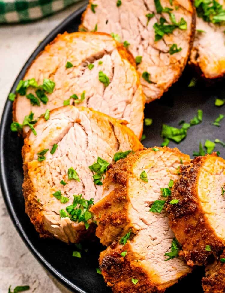 Sliced pork tenderloin on black plate