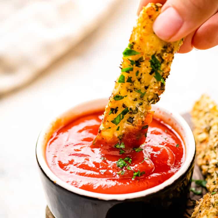 Hand dipping zucchini fry into a small bowl of ketchup