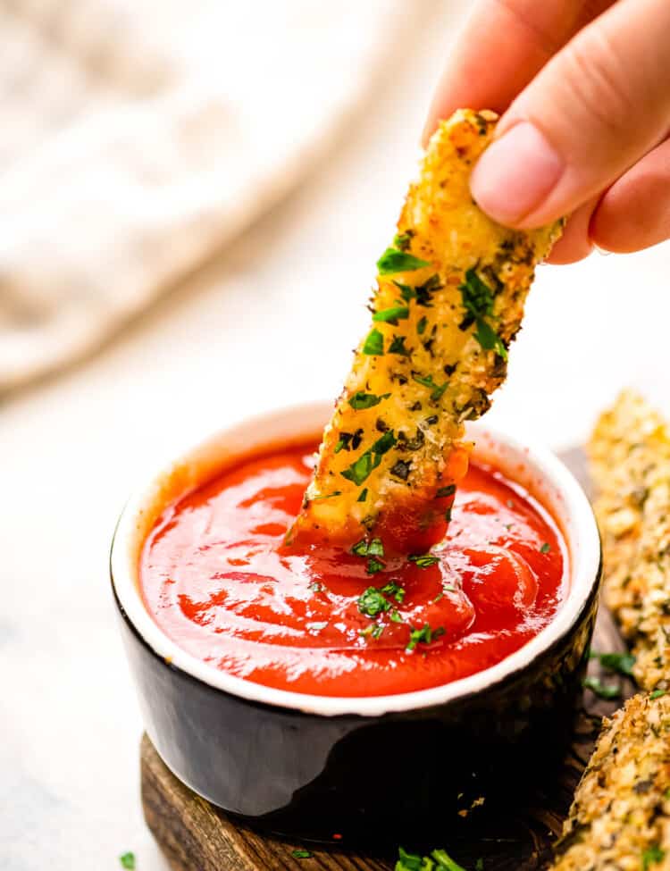 Hand dipping zucchini fry into a small bowl of ketchup